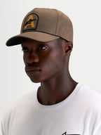 Alpinestars Czapka Acme Snapback, czapka sportowa w kolorze orzechowym z zakrzywionym daszkiem, usztywnioną koroną i naszywką z haftowanym logo Astars ze sznurkiem, prezentowana na modelu