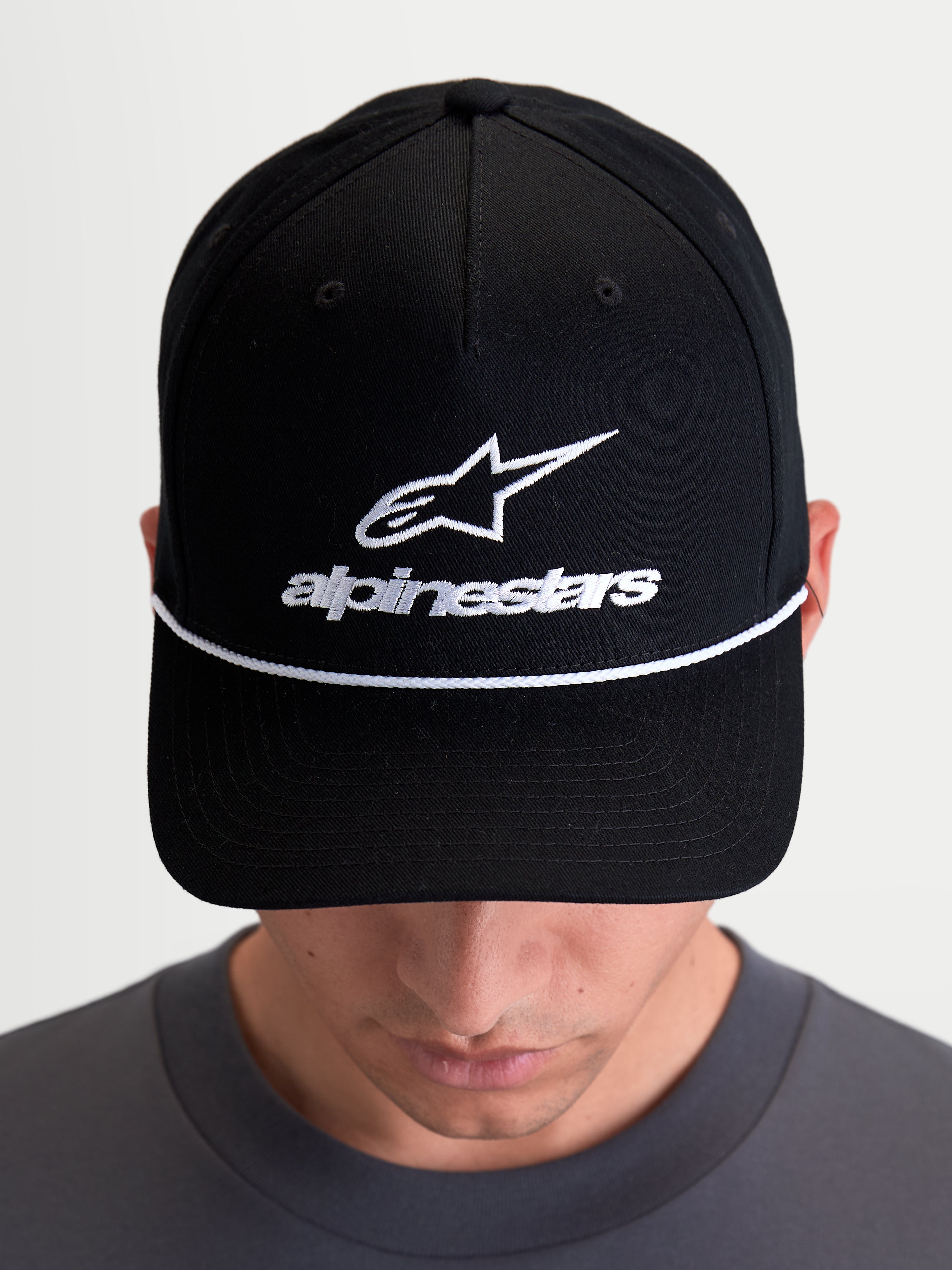 Alpinestars Czapka Combo Logo Snapback, czarna czapka z daszkiem na modelu, białe haftowane logo Astars na przodzie, biały dekoracyjny sznurek na zakrzywionym daszku, usztywniona korona, styl sportswear i motorsport