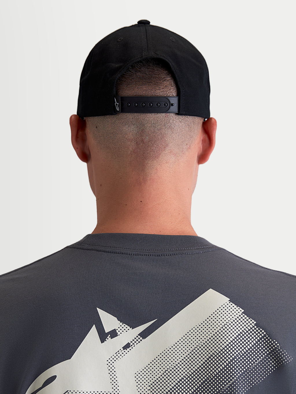 Alpinestars Combo Logo Snapback, czarna czapka z daszkiem, widok z tyłu na modelu pokazujący regulowane zapięcie snapback i mały biały detal logo, wytrzymały bawełniany kepr, odzież sportowa unisex