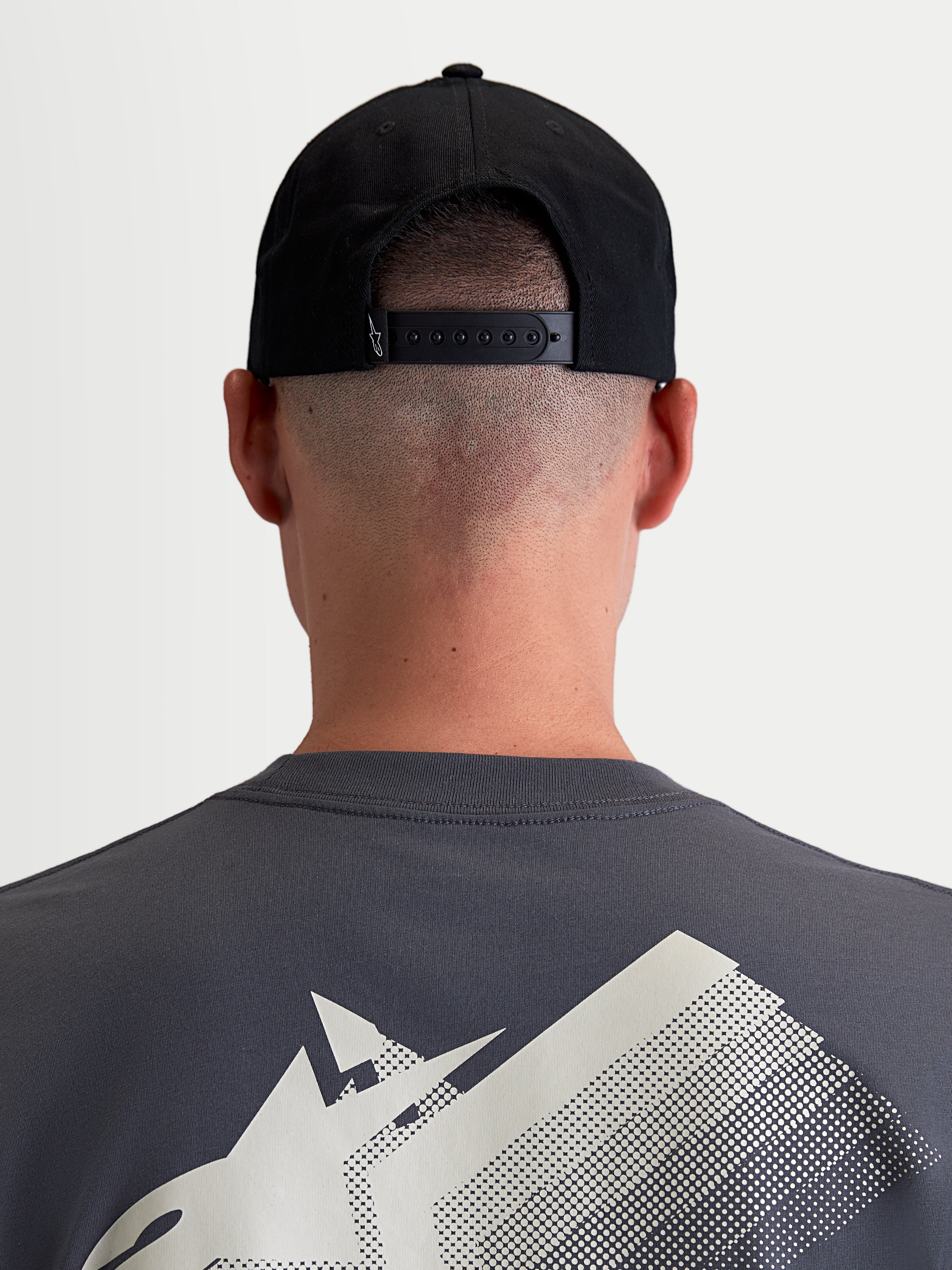 Alpinestars Combo Logo Snapback, czarna czapka z daszkiem, widok z tyłu na modelu pokazujący regulowane zapięcie snapback i mały biały detal logo, wytrzymały bawełniany kepr, odzież sportowa unisex