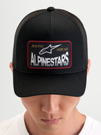 Alpinestars Hemmings Trucker, czapka z daszkiem sportswear, czarna, z przodu tkana naszywka z logo Alpinestars i z tyłu oddychające panele z siatki, na modelu