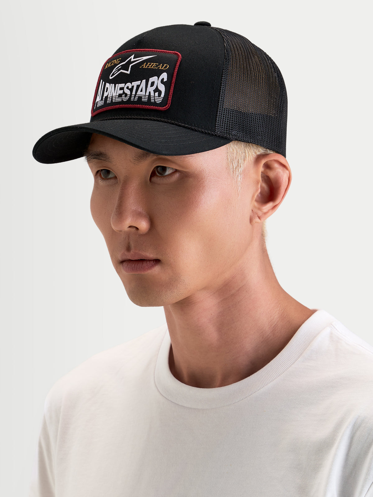 Alpinestars Hemmings Trucker, czapka z daszkiem sportswear, czarna z oddychającymi panelami z siatki z tyłu i tkaną naszywką z logo Alpinestars z przodu, na modelu