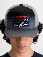 Alpinestars Czapka Z Daszkiem Gravel, sportowa czapka trucker, szara i czarna, tkana naszywka z przodu z napisem Racing Ahead i logo Astars, zakrzywiony daszek, tył z siatki, widok na modelu z przodu.