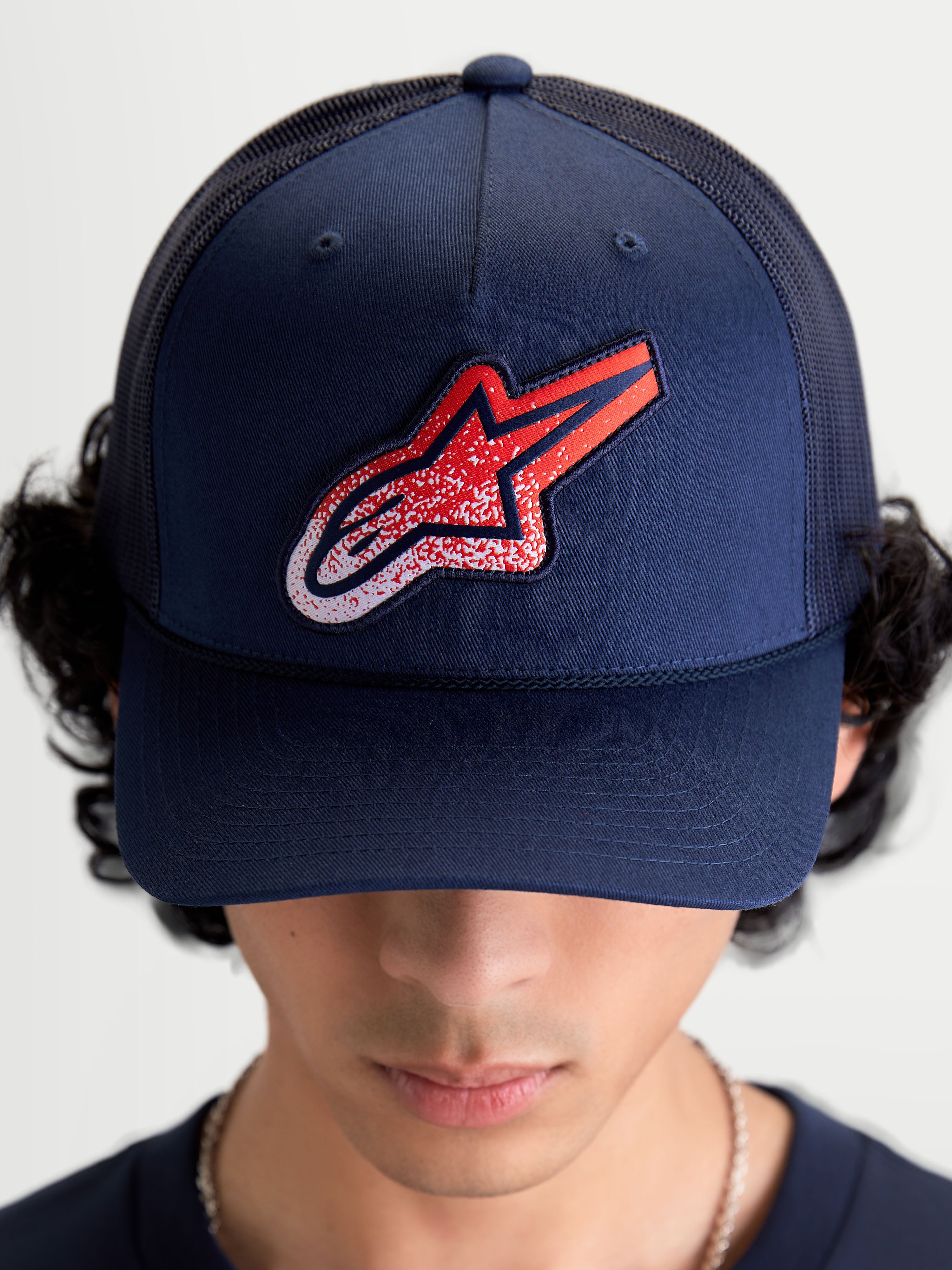 Alpinestars Czapka Z Daszkiem Meteorite, granatowa czapka z daszkiem, czerwone i białe logo Astars o fakturze żwiru, usztywniona korona i zakrzywiony daszek, widok z przodu na modelu.