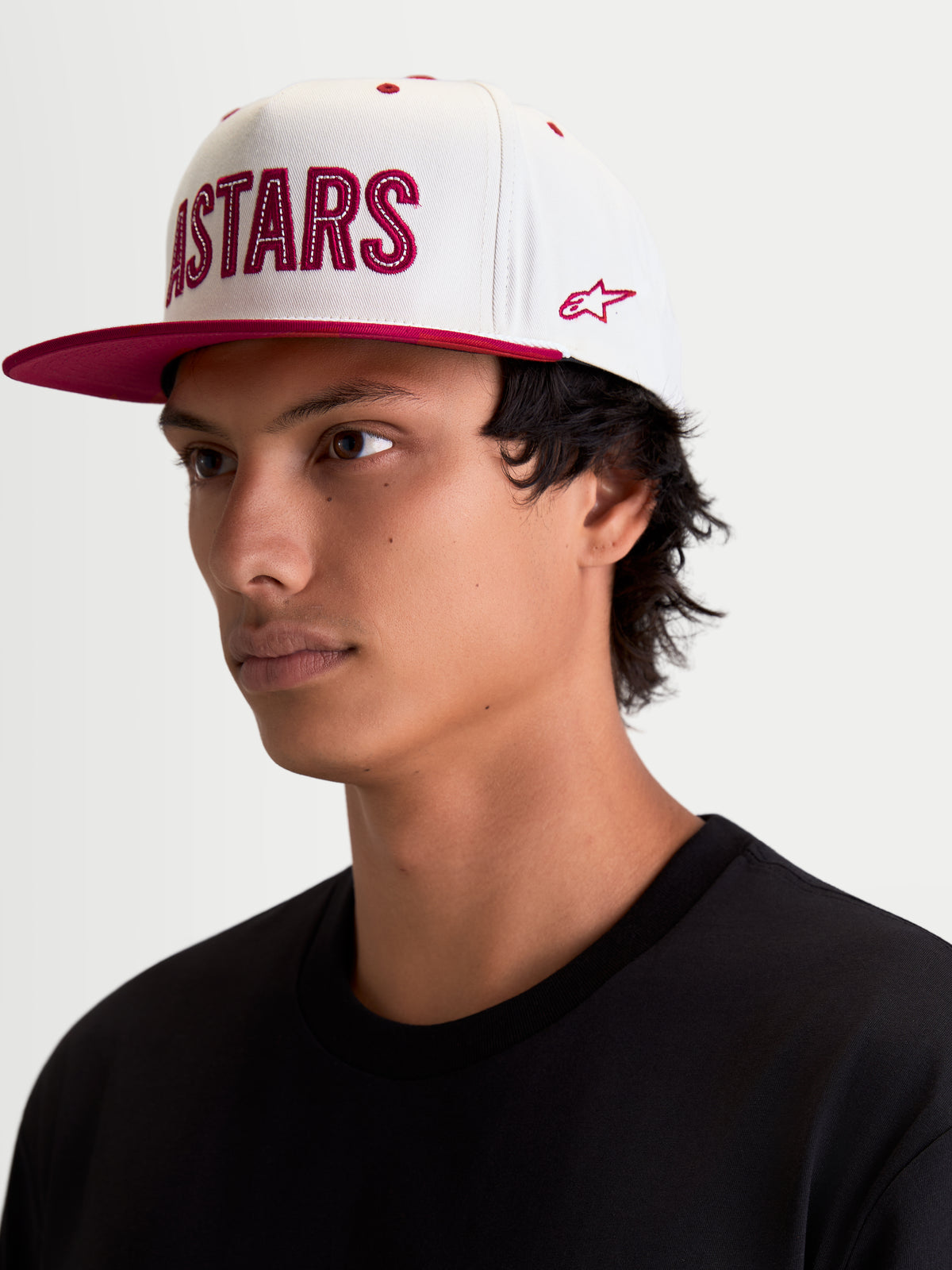 Alpinestars Czapka Stadium Snapback, biała i czerwona czapka z daszkiem typu lifestyle, płaski daszek, usztywniona korona, aplikacja z logo Astars z przodu z kontrastowym ściegiem i bocznym haftem, widok na modelu.