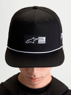 Alpinestars Label Snapback Hat, Sportswear Lifestyle Cap, Unisex, Black and White, Cotton Twill, featuring a structured crown, flat bill, white cord accent, and a front woven label patch with signature Alpinestars branding, shown on-model.