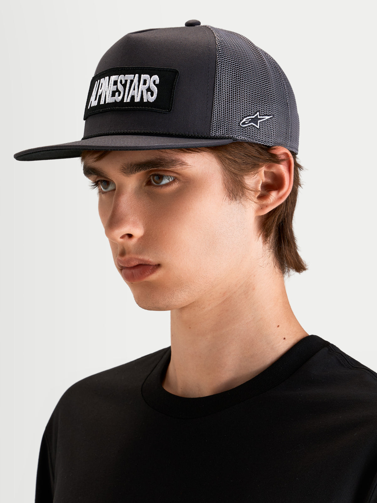 Alpinestars Ten Trucker, czapka z daszkiem sportowa w kolorze ciemnoszarym, na modelu, z haftowanym logo Alpinestars z przodu i logo Astars z boku