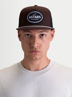 Alpinestars czapka z daszkiem Hotlink, brązowa i czarna czapka sportowa inspirowana motorsportem, usztywniona korona, płaski daszek z białym sznurkiem, tkana naszywka z logo Astars Worldwide, pokazana na modelu.