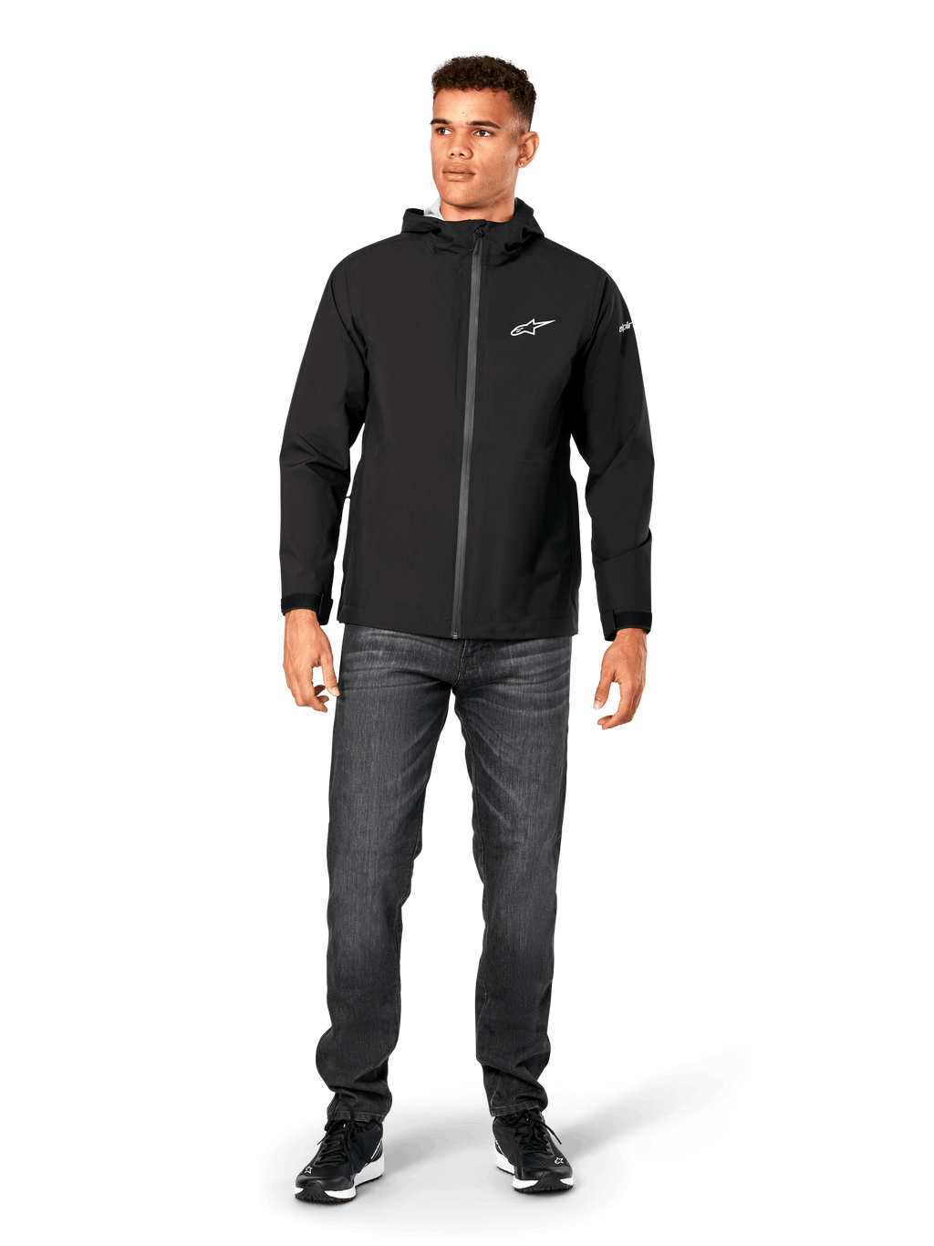 Kurtka przeciwdeszczowa Alpinestars Kascade, męska kurtka przeciwdeszczowa, czarna, noszona z ciemnoszarymi jeansami i czarnymi sneakersami, model z kapturem, powlekany zamek z przodu, białe logo Alpinestars na piersi, streetwear inspirowany motorsportem