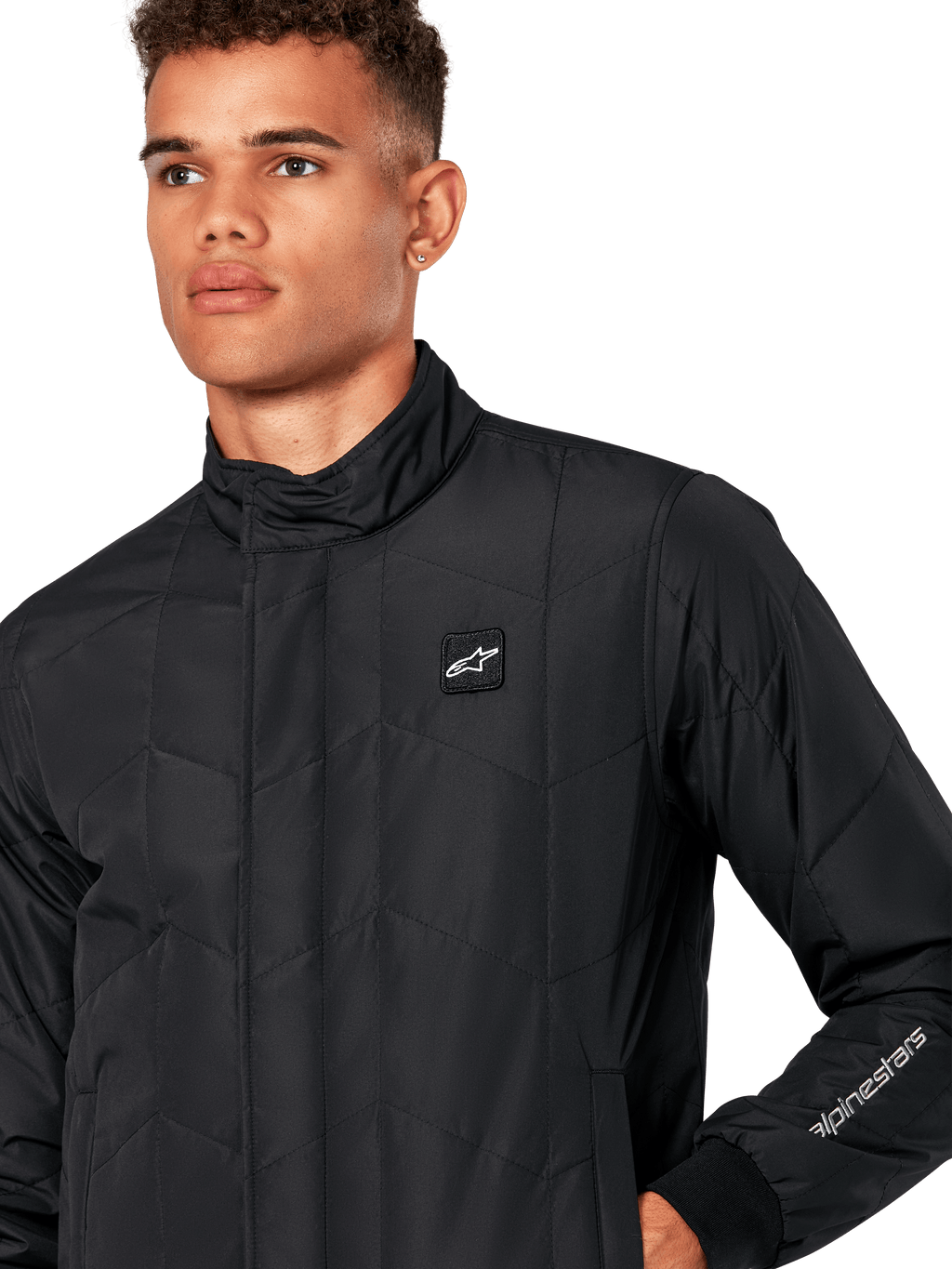 Kurtka Alpinestars Precedent, męska pikowana kurtka sportowa w kolorze czarnym, zbliżenie pokazujące niski kołnierz, naszywkę z logo na piersi i haft na rękawie, kultowy skośny wzór pikowania inspirowany sportami motorowymi