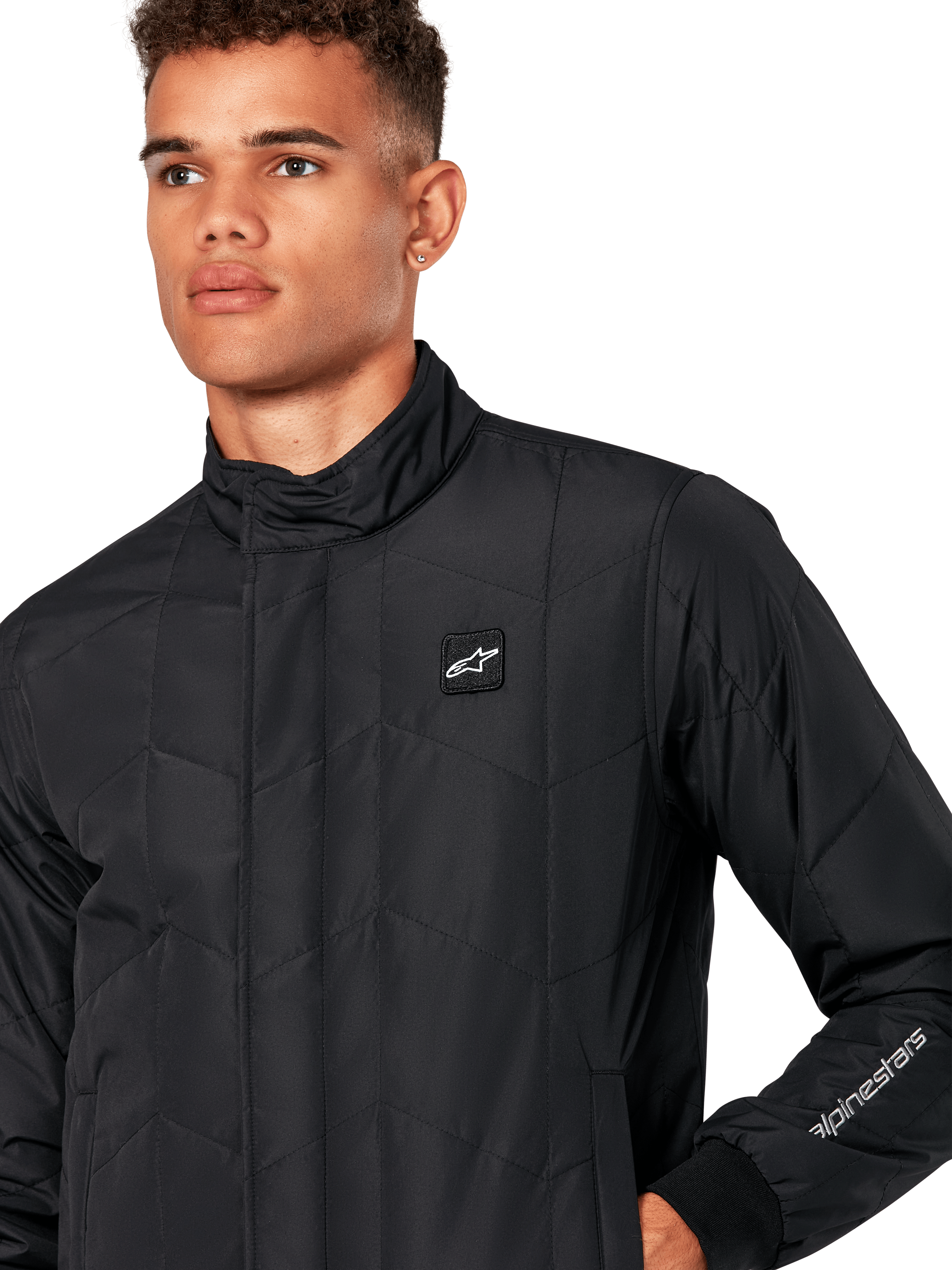 Kurtka Alpinestars Precedent, męska pikowana kurtka sportowa w kolorze czarnym, zbliżenie pokazujące niski kołnierz, naszywkę z logo na piersi i haft na rękawie, kultowy skośny wzór pikowania inspirowany sportami motorowymi