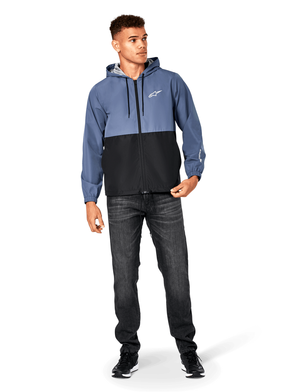 Kurtka Alpinestars Speeder Windbreaker, stalowoniebieska i czarna, lekka wiatrówka z kapturem i siatkową podszewką, białe logo z gwiazdą na piersi, noszona z czarnymi dżinsami i sneakersami, casualowy design w stylu motorsport streetwear.