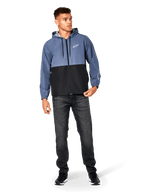 Kurtka Alpinestars Speeder Windbreaker, stalowoniebieska i czarna, lekka wiatrówka z kapturem i siatkową podszewką, białe logo z gwiazdą na piersi, noszona z czarnymi dżinsami i sneakersami, casualowy design w stylu motorsport streetwear.