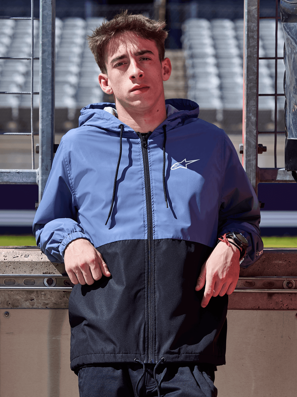 Kurtka Alpinestars Speeder Windbreaker, stalowoniebieska i czarna, wiatrówka z kapturem o panelowej konstrukcji, białe logo na klatce piersiowej, odzież lifestylowa noszona na torze wyścigowym