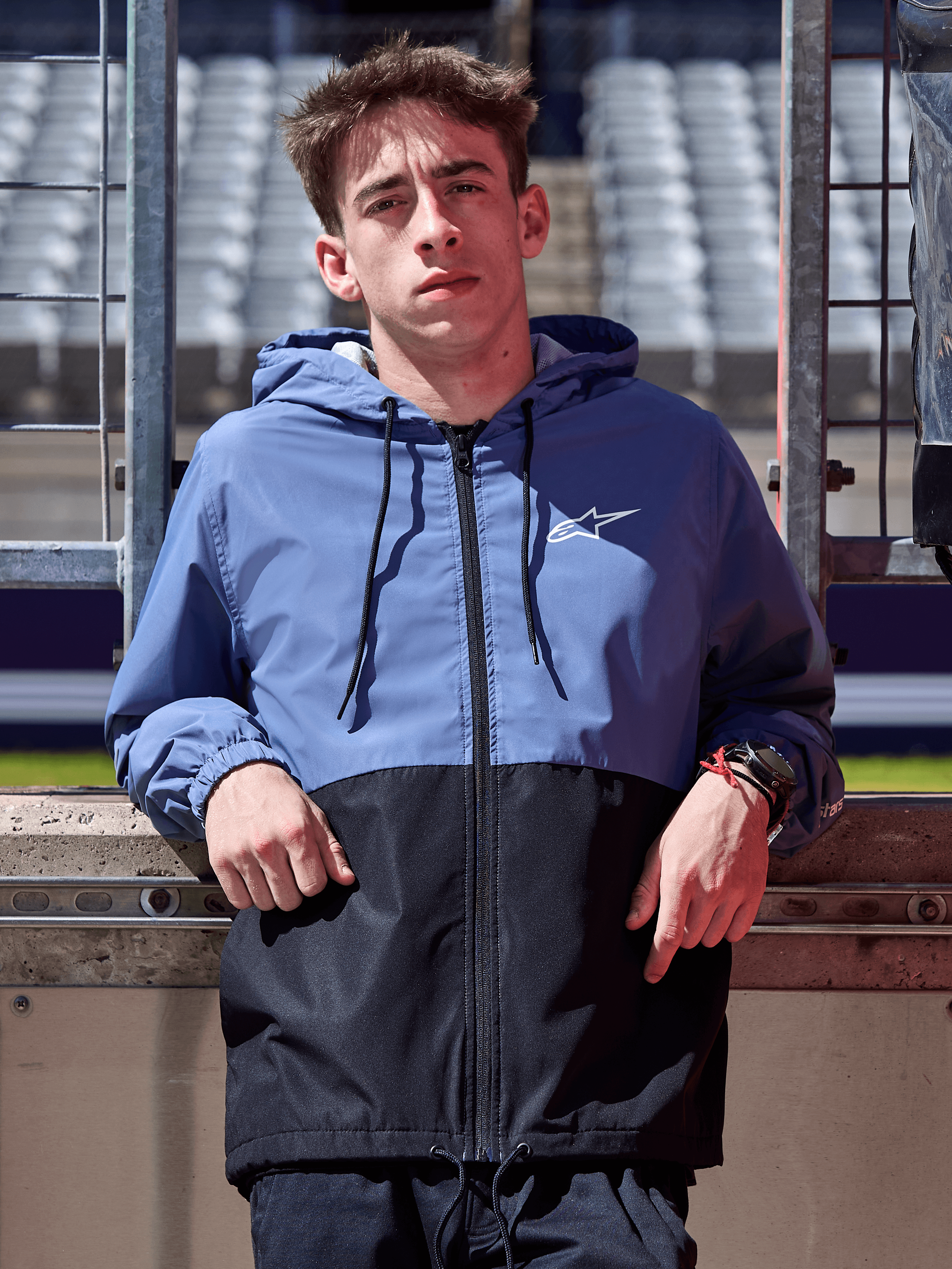 Kurtka Alpinestars Speeder Windbreaker, stalowoniebieska i czarna, wiatrówka z kapturem o panelowej konstrukcji, białe logo na klatce piersiowej, odzież lifestylowa noszona na torze wyścigowym