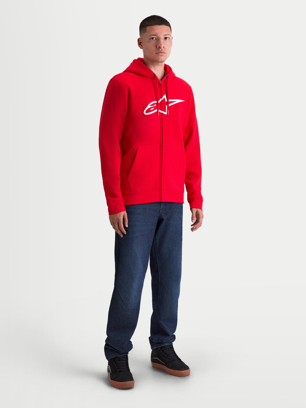 Alpinestars Bluza z kapturem Ageless Zip V3, czerwona męska bluza polarowa na zamek, duże białe logo na piersi, casualowa odzież sportowa w stylu motorsport, model ubrany w czerwony polar z kapturem i dżinsy.
