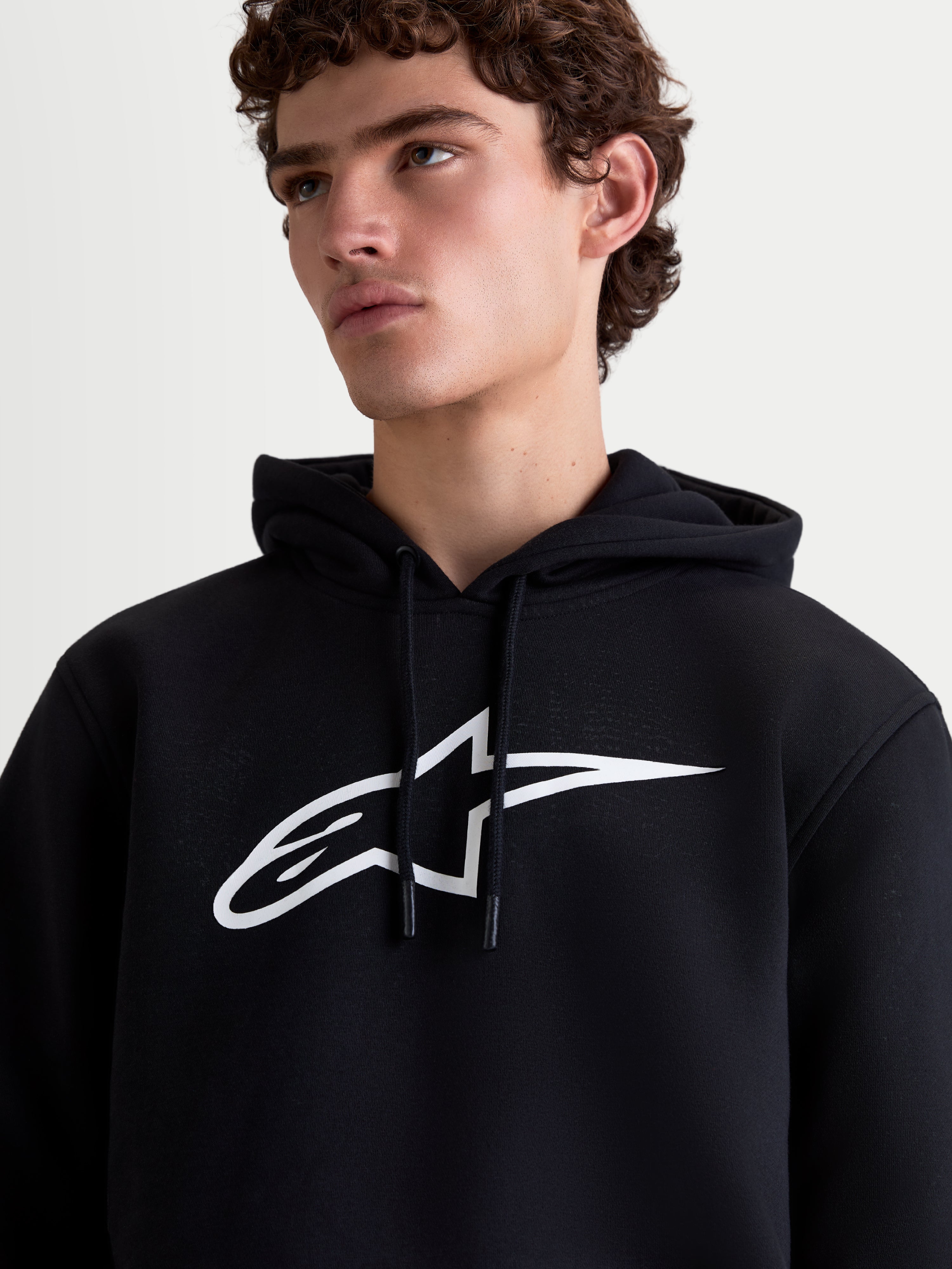 Alpinestars Ageless V3, męska bluza z kapturem typu pullover, czarna i biała, duże białe logo na klatce piersiowej, polarowa odzież sportowa, zbliżenie na modelu.