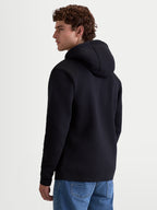 Alpinestars Ageless V3 Hoodie, męska bluza z kapturem typu pullover, czarna, miękka polarowa mieszanka bawełny i poliestru z recyklingu, widok z tyłu na modela prezentujący kaptur i ściągacze przy mankietach, odzież sportowa lifestyle.