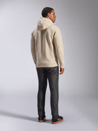 Alpinestars Ageless V3 Hoodie, codzienna polarowa bluza z kapturem w kolorze złamanej bieli widoczna od tyłu, prążkowane mankiety i dolny brzeg, noszona z ciemnymi dżinsami o kroju slim i czarnymi sneakersami Alpinestars