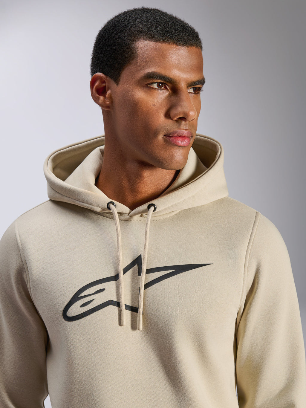 Alpinestars Ageless V3 Hoodie, sportowa odzież casual, złamana biel z czarnym haftowanym logo gwiazdy Alpinestars, kaptur ze sznurkiem, zbliżenie na modelu, miękki polar, nowoczesny design inspirowany motorsportem