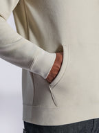 Alpinestars Ageless V3 Hoodie, zbliżenie na przednią kieszeń typu kangurka i prążkowany mankiet, polar w kolorze off-white, casualowy streetwear inspirowany sportami motorowymi