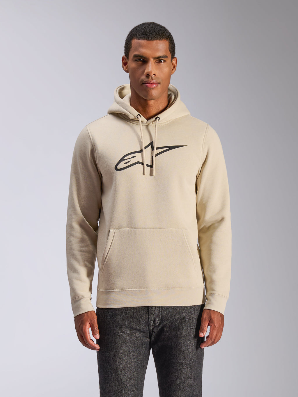 Alpinestars Ageless V3 Hoodie, bluza z kapturem w stylu streetwear, kolor złamanej bieli z czarnym haftowanym logo, model wkładany przez głowę z kieszenią typu kangurka, prezentowana przez modela w ciemnych spodniach, nowoczesny design inspirowany motorsportem