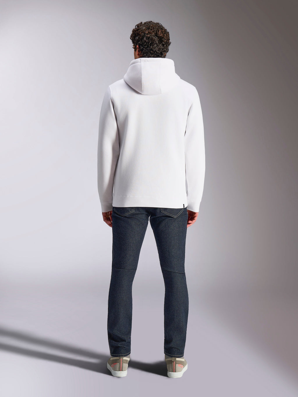 Bluza z kapturem Alpinestars Blaze V3, biała sportowa bluza lifestyle, widok z tyłu, minimalistyczny design ze ściągaczami na mankietach i dole, zestawiona z ciemnoniebieskimi dżinsami i sneakersami, nowoczesna odzież inspirowana sportami motorowymi