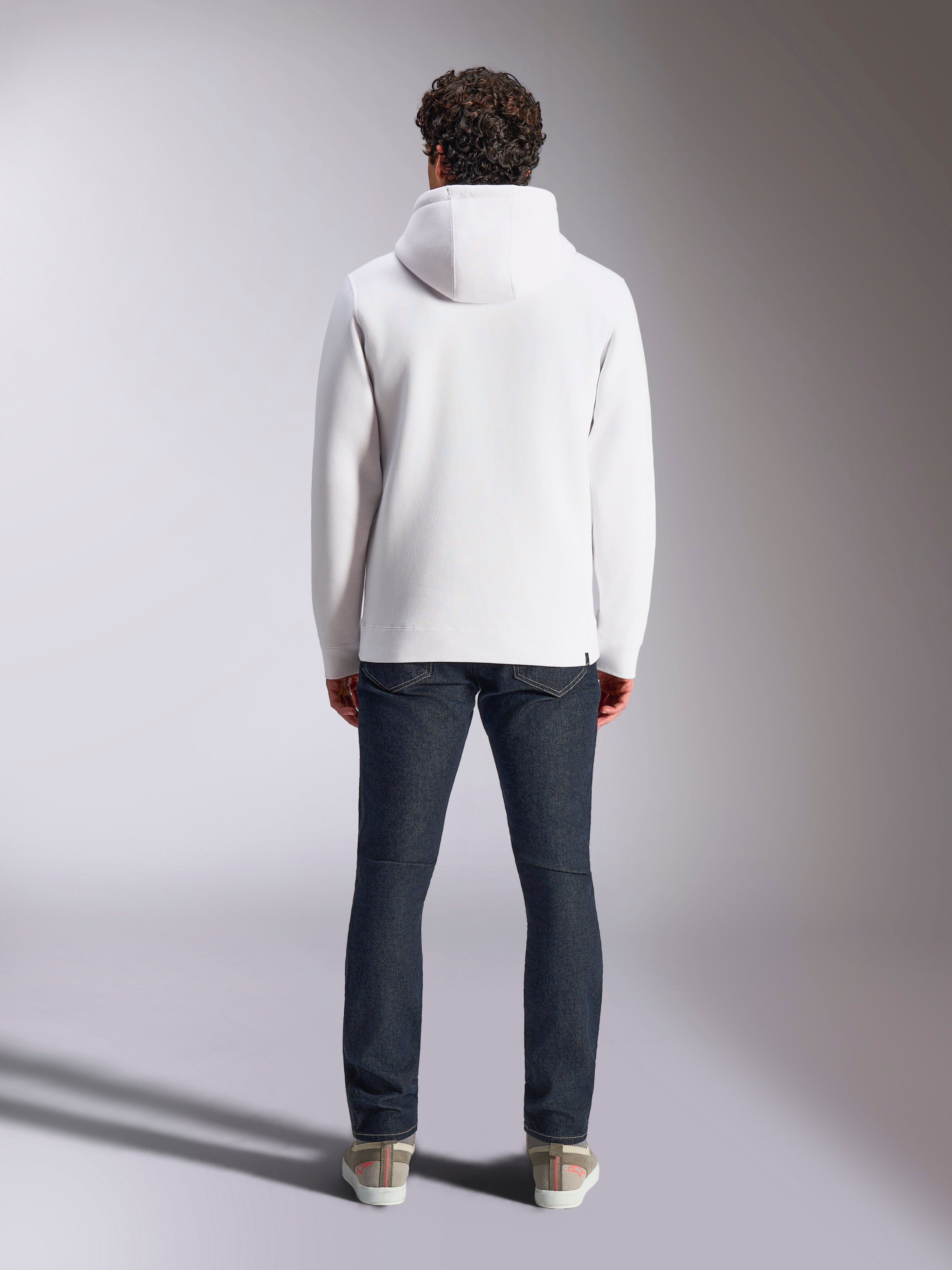 Bluza z kapturem Alpinestars Blaze V3, biała sportowa bluza lifestyle, widok z tyłu, minimalistyczny design ze ściągaczami na mankietach i dole, zestawiona z ciemnoniebieskimi dżinsami i sneakersami, nowoczesna odzież inspirowana sportami motorowymi