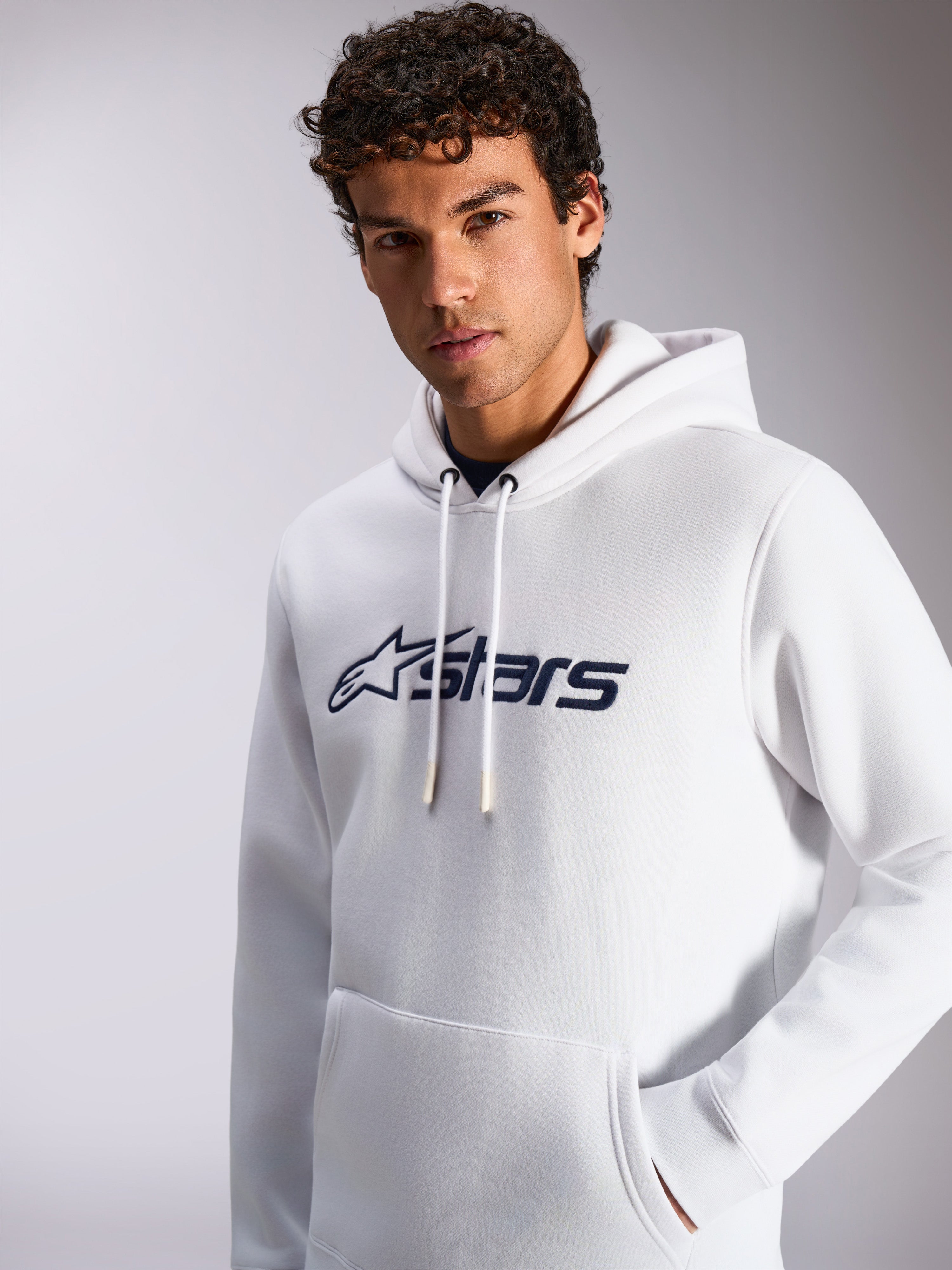 Alpinestars Blaze V3 Hoodie, biało-granatowa, prezentowana na modelu, codzienna odzież sportowa, granatowe logo Alpinestars z przodu, kaptur ze sznurkiem, kieszeń typu kangur, nowoczesny lifestylowy design
