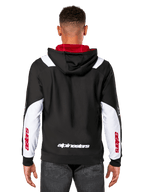 Alpinestars Sessions V3 Hoodie, widok z tyłu, czarna z białymi panelami na rękawach i czerwoną podszewką kaptura, z białym napisem z tyłu i czerwonym brandingiem na rękawach, codzienna odzież streetwearowa inspirowana sportami motorowymi