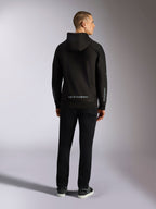 Bluza z kapturem Alpinestars Sessions V3, casualowa odzież uliczna, czarna z szarym napisem Alpinestars na dole pleców i brandingiem „astars” na rękawach, widok z tyłu na męskiego modelu w bluzie i czarnych spodniach, nowoczesny design inspirowany sportami motorowymi