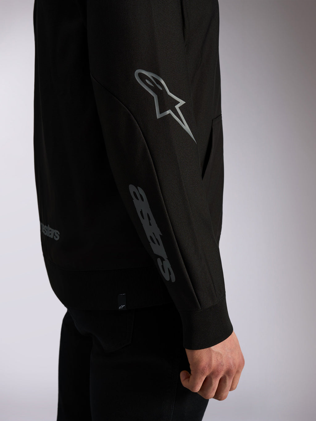 Bluza z kapturem Alpinestars Sessions V3, czarna odzież streetwearowa, zbliżenie na rękaw z szarym logo Astars na łokciu i logotypem na przedramieniu, prążkowane ściągacze, design inspirowany sportami motorowymi