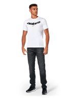 Alpinestars Elliptic CSF Tee, koszulka z krótkim rękawem, biała, czarne łukowate logo Astars z pomarańczowym symbolem gwiazdy, model w czarnych jeansach i sneakersach, codzienna odzież streetwearowa w stylu motorsport