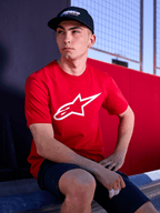 Czapka Alpinestars Profile, czarna, zdjęcie typu lifestyle przedstawiające mężczyznę w czapce z zakrzywionym daszkiem i czerwonym t-shircie z białym logo Alpinestars, codzienna odzież uliczna inspirowana sportami motorowymi