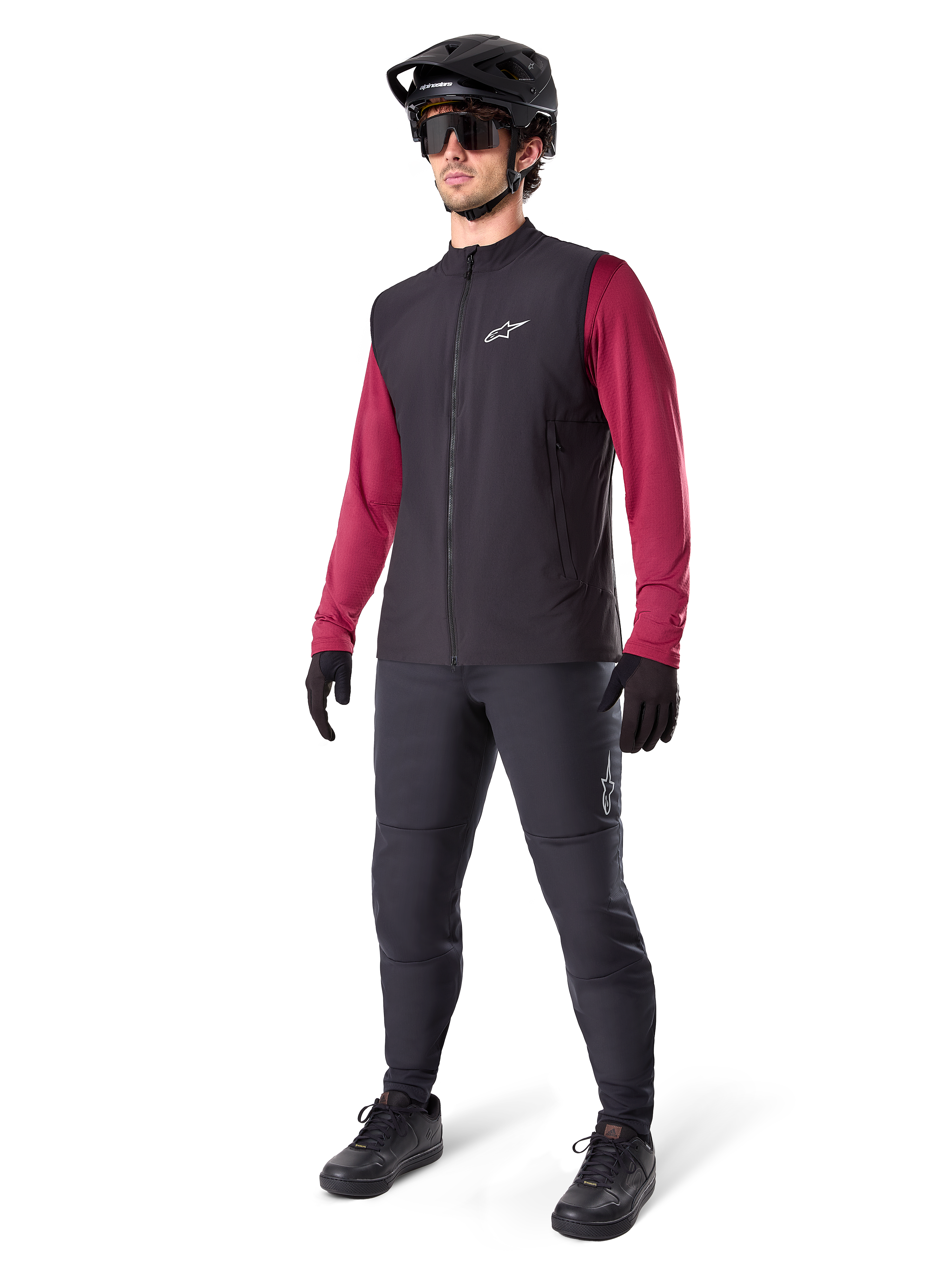 Alpinestars A-Dura Thermal Vest, czarna kamizelka rowerowa, noszona przez rowerzystę na bordową koszulkę z długim rękawem i czarne spodnie, z czarnym kaskiem MTB i rękawicami, zaprojektowana do jazdy na rowerze górskim w chłodne dni