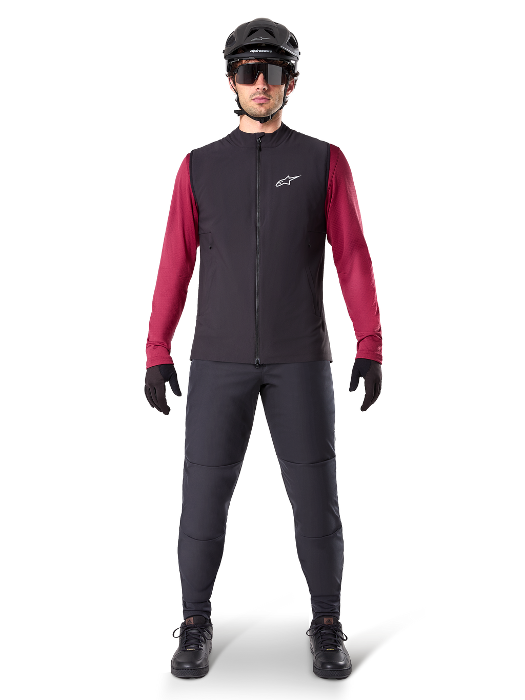 Kamizelka Alpinestars A-Dura Thermal, czarna kamizelka rowerowa założona na bordową koszulkę z długim rękawem, ciemnoszare spodnie MTB, czarny kask i okulary przeciwsłoneczne, techniczna odzież na rower górski do jazdy w zimne dni