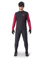 Kamizelka Alpinestars A-Dura Thermal, czarna kamizelka rowerowa założona na bordową koszulkę z długim rękawem, ciemnoszare spodnie MTB, czarny kask i okulary przeciwsłoneczne, techniczna odzież na rower górski do jazdy w zimne dni