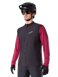 Alpinestars A-Dura Thermal Vest, czarna rowerowa kamizelka termiczna, noszona na bordowej koszulce z długim rękawem, z białym logo na piersi, w zestawie z czarnym kaskiem MTB i okularami przeciwsłonecznymi, izolująca warstwa techniczna do kolarstwa górskiego