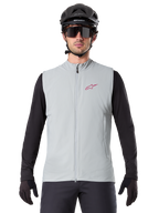 Alpinestars A-Dura Thermal Vest, kamizelka rowerowa, szary Titanium, noszona z czarną koszulką z długim rękawem i czarnym kaskiem rowerowym, czerwone logo gwiazdy Alpinestars na piersi, lekka i ocieplana konstrukcja do kolarstwa górskiego