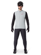 Kamizelka termiczna Alpinestars A-Dura, kamizelka rowerowa, szary Titanium, zestawiona z czarną koszulką z długim rękawem i czarnymi spodniami, czarny kask i okulary przeciwsłoneczne, czerwone logo Alpinestars, lekka izolacja termiczna do jazdy na rowerze górskim