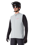 Kamizelka termiczna Alpinestars A-Dura, Titanium Gray, rowerowa kamizelka ocieplana, założona na czarną koszulkę z długim rękawem, z czarnym kaskiem MTB i rękawiczkami, różowe logo na piersi, pionowe boczne kieszenie na zamek