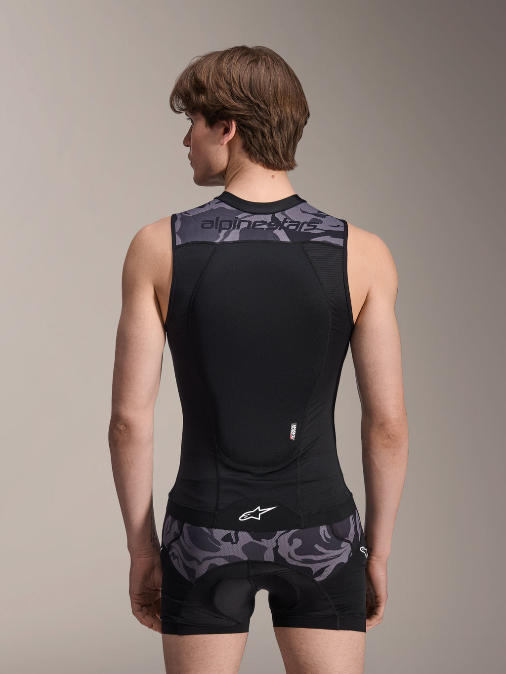 Alpinestars A-Motion Plasma Protection Vest, Black Camo, widok od tyłu na modelu, oddychająca konstrukcja z siatki ze zintegrowanym ochraniaczem pleców Nucleon Plasma, szare akcenty kamuflażowe na ramionach i w pasie, logo Alpinestars