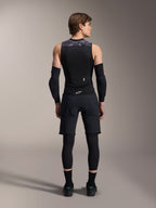 Kamizelka ochronna Alpinestars A-Motion Plasma, widok z tyłu, czarna z szarymi akcentami camo na ramionach, model w czarnych ochraniaczach łokci, spodenkach rowerowych na legginsach i czarnych butach, prezentacja zintegrowanego ochraniacza pleców