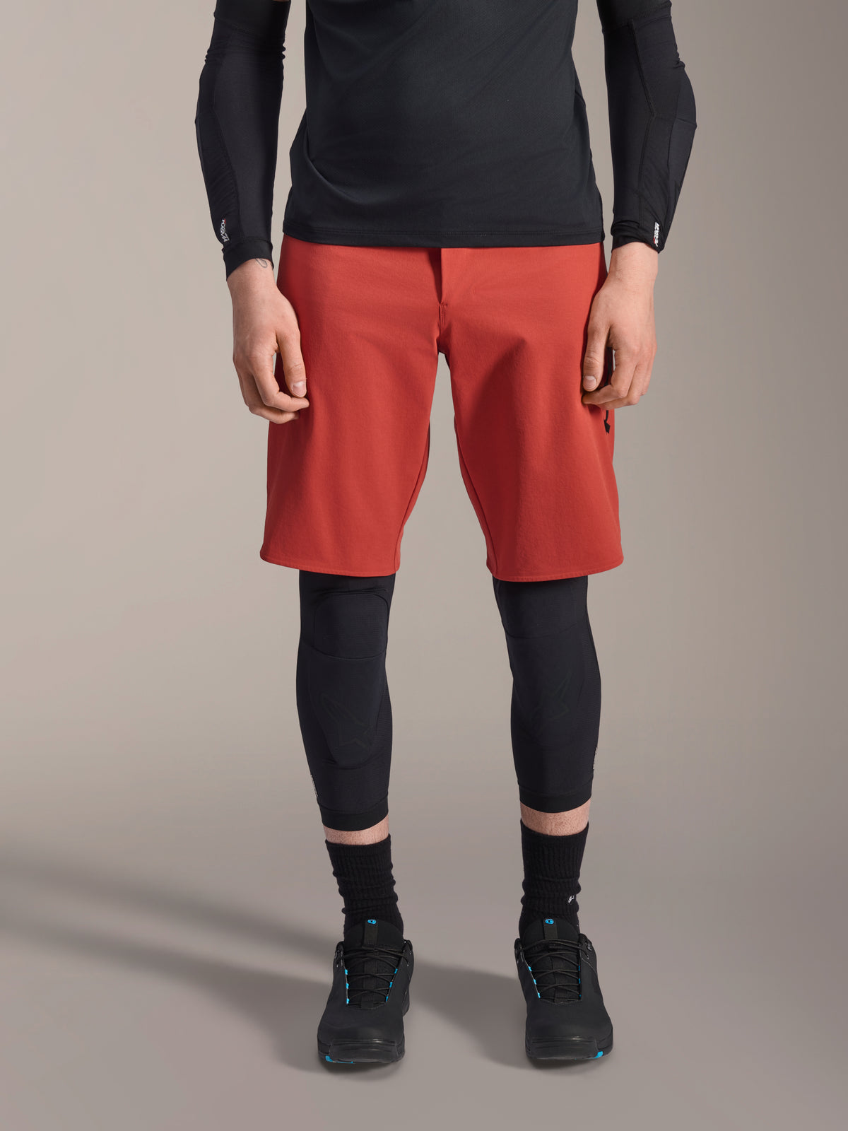 Alpinestars A-Motion Plasma Knee Sleeve, Black MTB knee protector, worn with red shorts and black long-sleeve top, slim-profile ergonomic design, lightweight mesh construction for off-road riding
