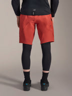 Alpinestars A-Motion Plasma Knee Sleeve, czarne ochraniacze kolan MTB, widok z tyłu, noszone pod czerwonymi spodenkami rowerowymi, czarna koszulka i techniczne buty rowerowe, sprzęt ochronny do kolarstwa górskiego