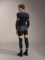 Model w bokserkach ochronnych Alpinestars A-Motion Plasma w kolorze Black Camo i pasującej kurtce ochronnej A-Motion Plasma, widok z tyłu, szary wzór kamuflażu, ochraniacze łokci, ochraniacze kolan, buty rowerowe, kompletny zestaw ochronny MTB