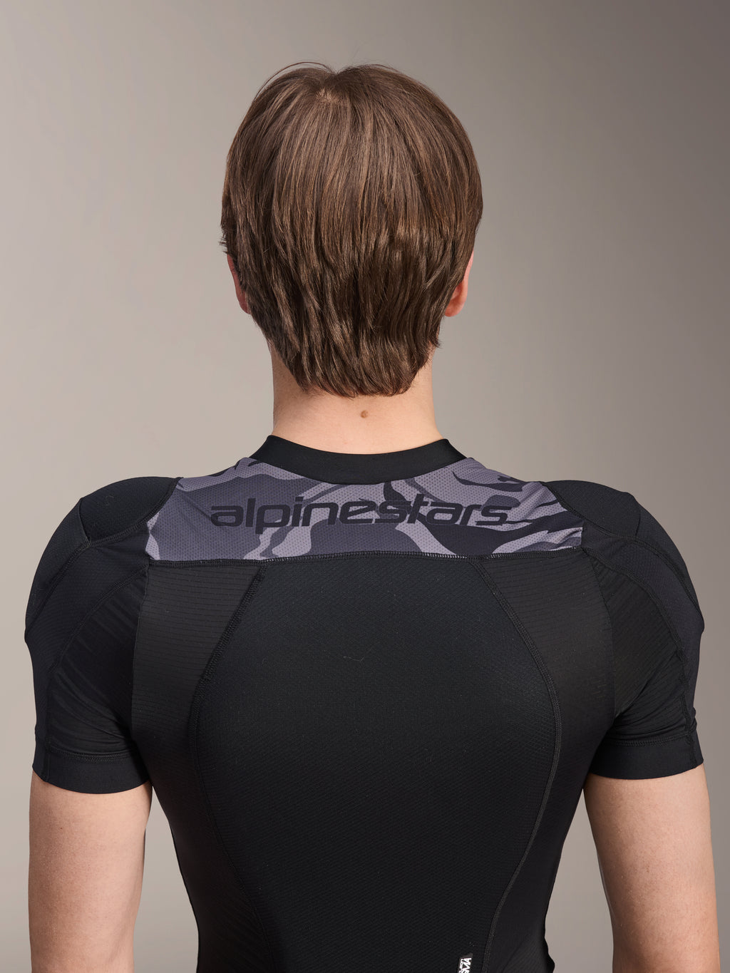 Alpinestars A-Motion Plasma Protection Jacket - Short Sleeve, widok z tyłu na górną część tułowia, czarna z szarym panelem moro na ramionach z logo Alpinestars, oddychająca konstrukcja z elastycznej siatki dla ochrony MTB