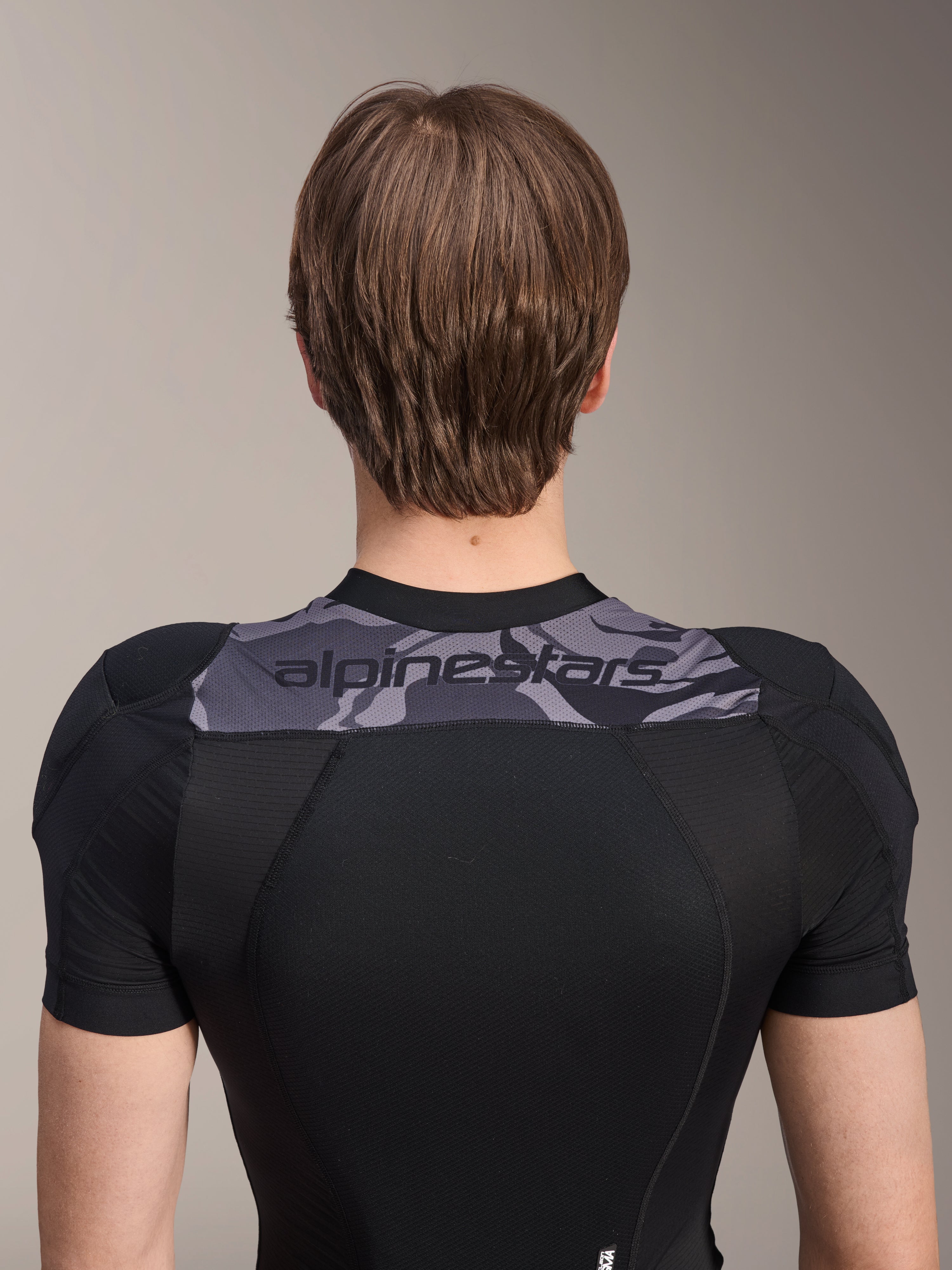 Alpinestars A-Motion Plasma Protection Jacket - Short Sleeve, widok z tyłu na górną część tułowia, czarna z szarym panelem moro na ramionach z logo Alpinestars, oddychająca konstrukcja z elastycznej siatki dla ochrony MTB
