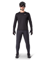Alpinestars A-Dura Thermal Pant, czarne spodnie rowerowe MTB, noszone przez rowerzystę w kompletnym stroju z czarną koszulką z długim rękawem, kaskiem i okularami, wytrzymałe spodnie o regularnym kroju do jazdy w chłodne dni