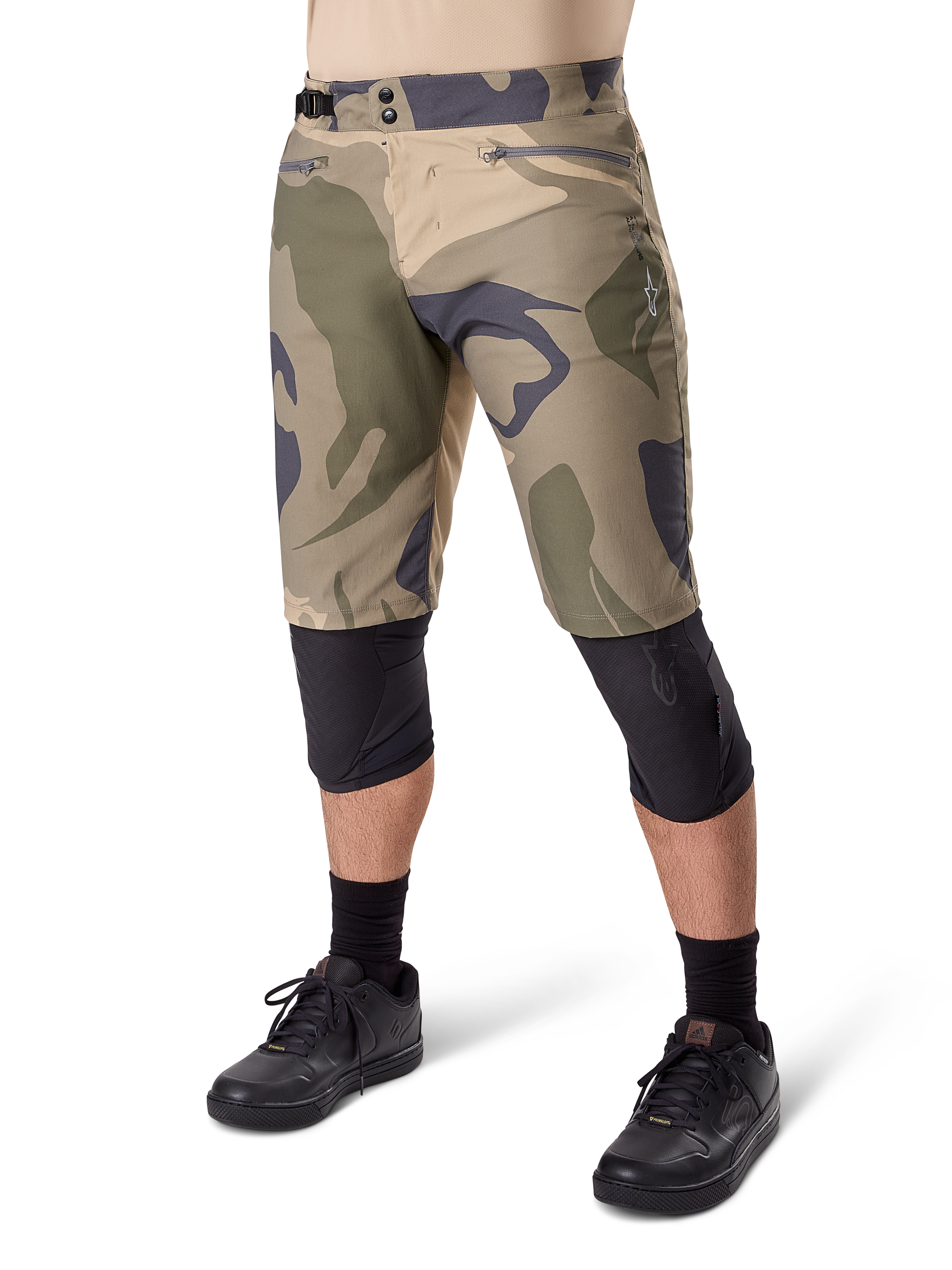 Alpinestars A-Dura Camo Liner Short, spodenki rowerowe MTB, brązowy wzór camo, widok z przodu prezentujący kieszenie zapinane na zamek i boczne regulatory w pasie, noszone z czarnymi ochraniaczami na kolana i czarnymi butami rowerowymi, wytrzymała odzież MTB